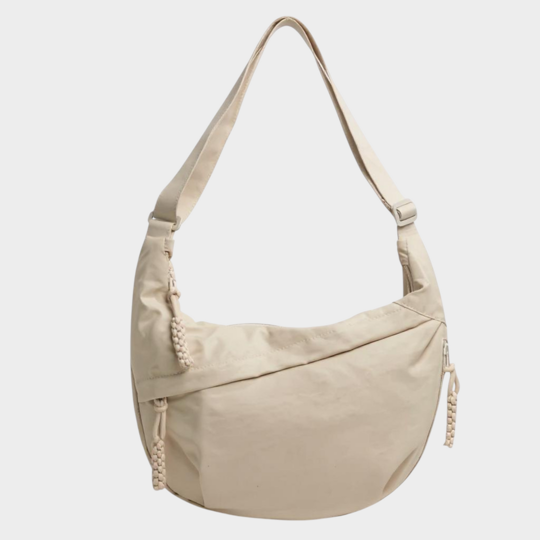 Zane & Inese Serafīna beige nylon crescent shoulder bag with adjustable strap and practical zipper compartments.