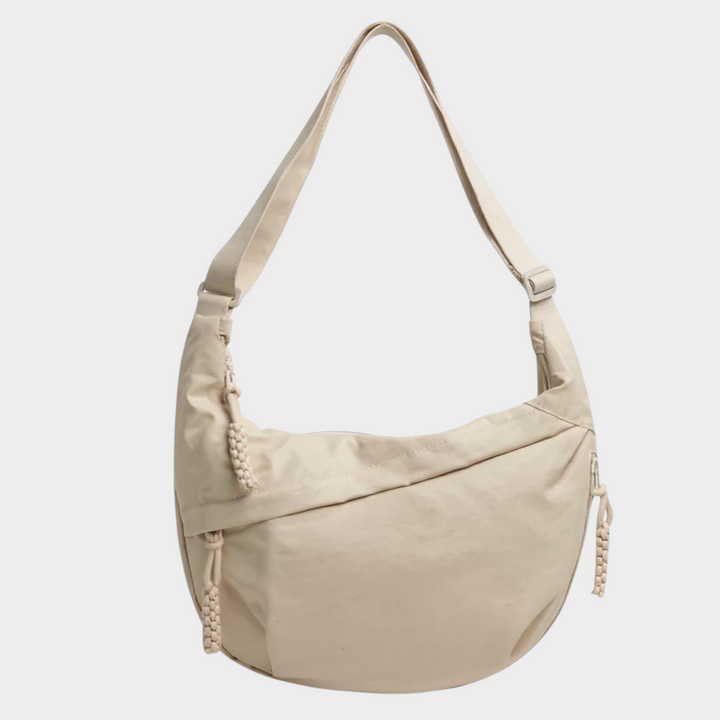 Zane & Inese Serafīna beige nylon crescent shoulder bag with adjustable strap and practical zipper compartments.
