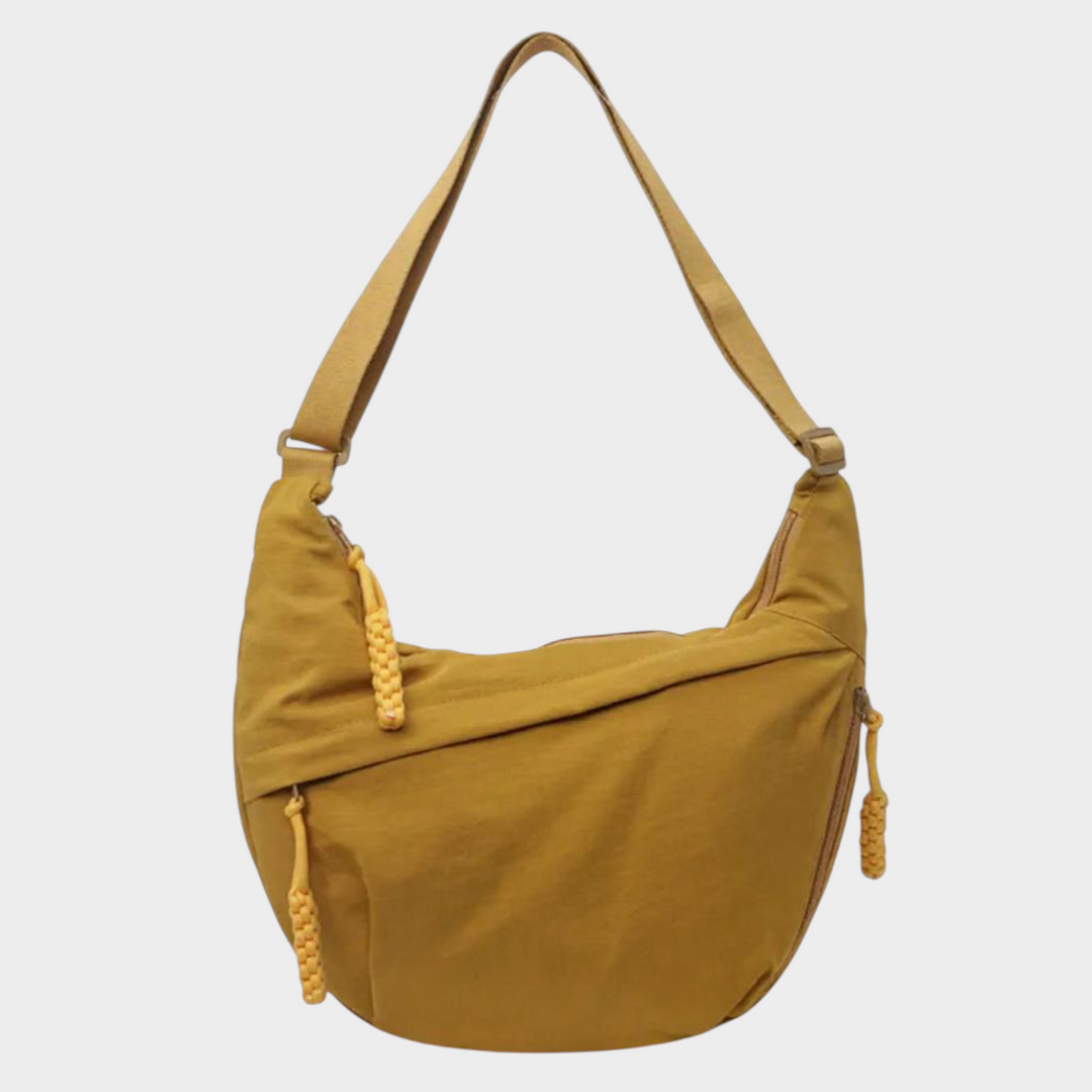 Zane & Inese Serafīna crescent-shaped mustard yellow nylon shoulder bag with adjustable strap and zipper details.