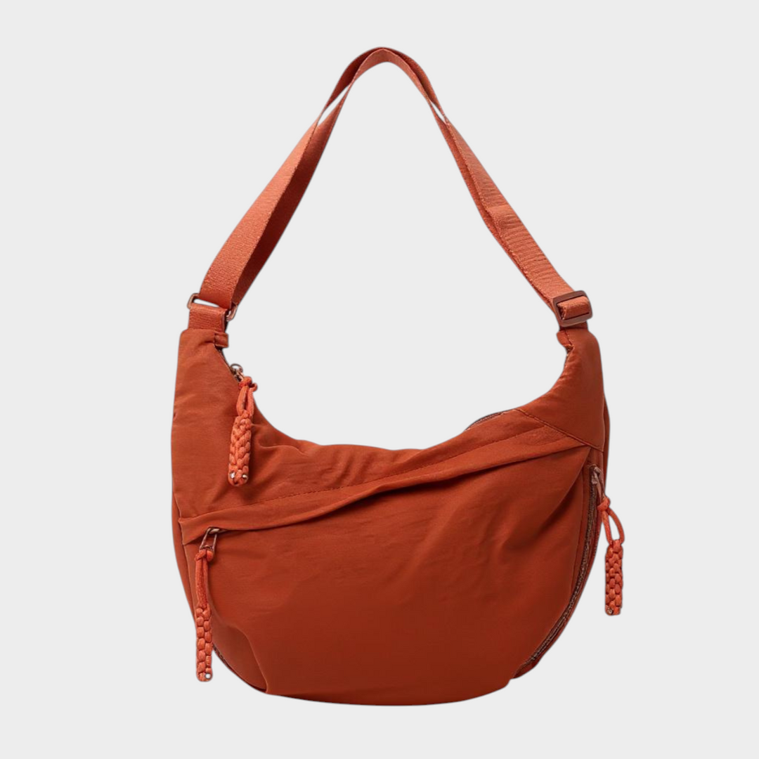 Zane & Inese Serafīna orange nylon crescent shoulder bag with adjustable strap and practical zipper compartments.