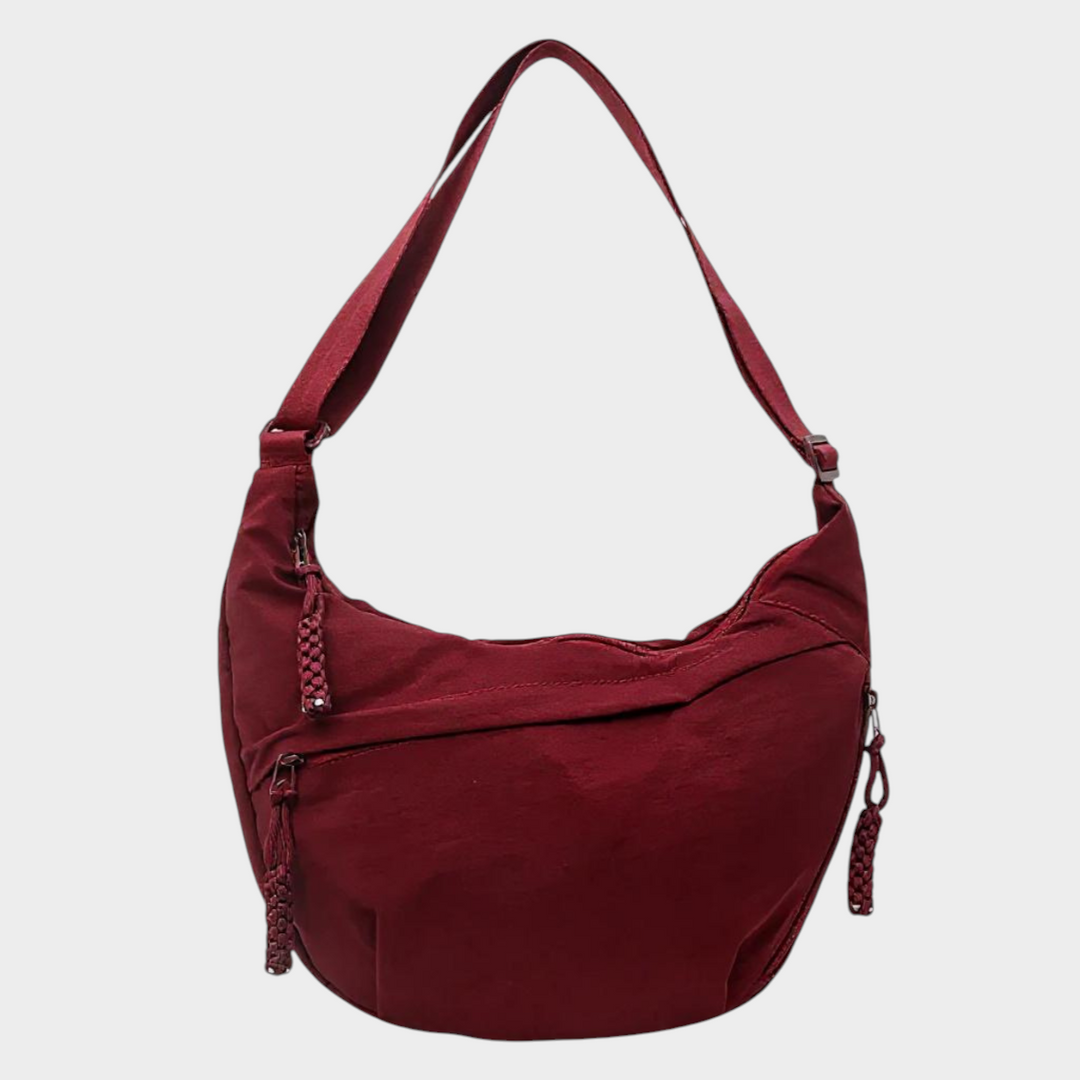 Zane & Inese Serafīna red nylon crescent shoulder bag with adjustable strap and multiple zippered compartments.