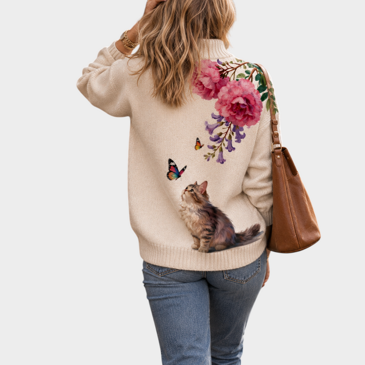 Zane & Inese cream high-neck sweater featuring a cat and floral embroidery, worn by a woman with a brown leather bag.