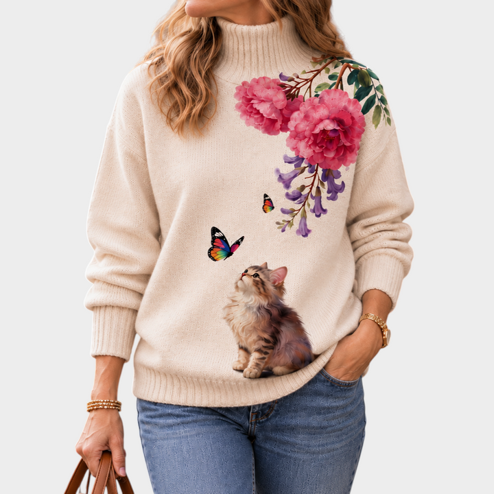 Zane & Inese cream high-neck sweater featuring a kitten, butterflies, and pink floral embroidery, worn with jeans.